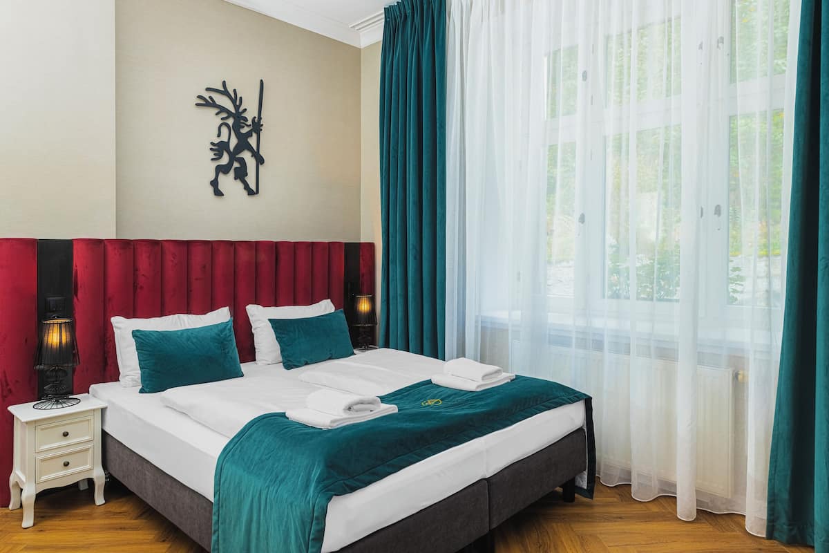 Quarto de hotel com cama, mesa de cabeceira, abajur e janela com cortinas.