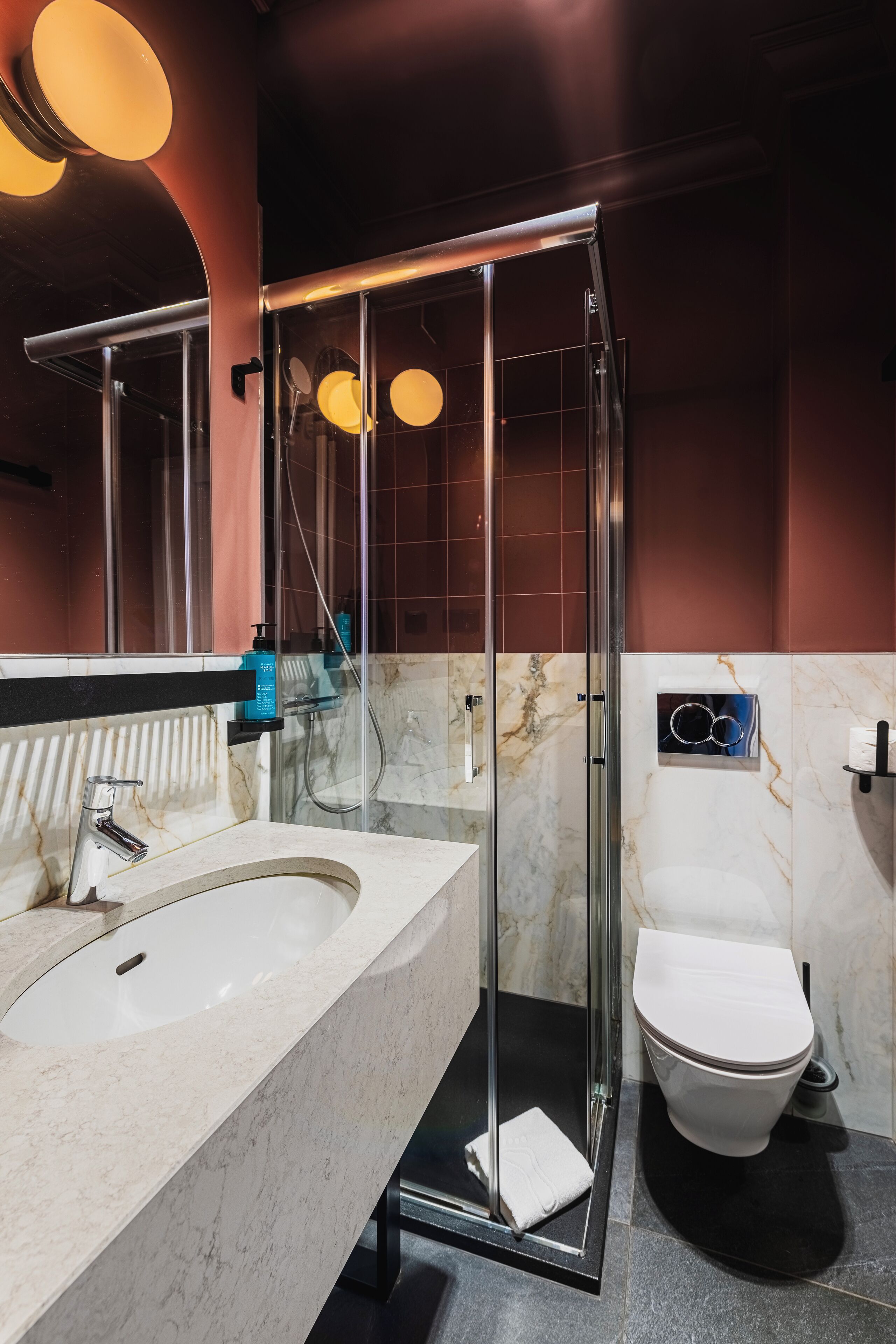 A modern bathroom with a glass-enclosed shower, a marble sink, and a white toilet.