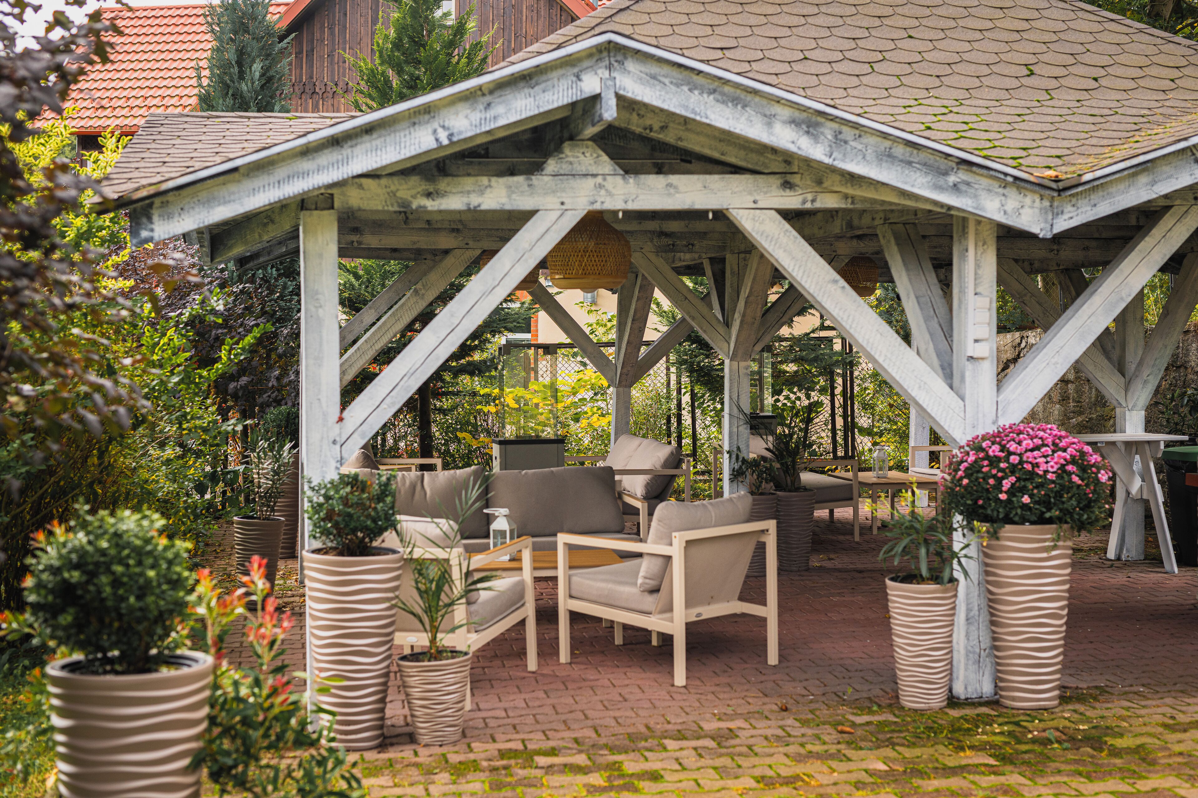 Een overdekt terras met een bakstenen vloer, omgeven door potplanten en een houten pergola.
