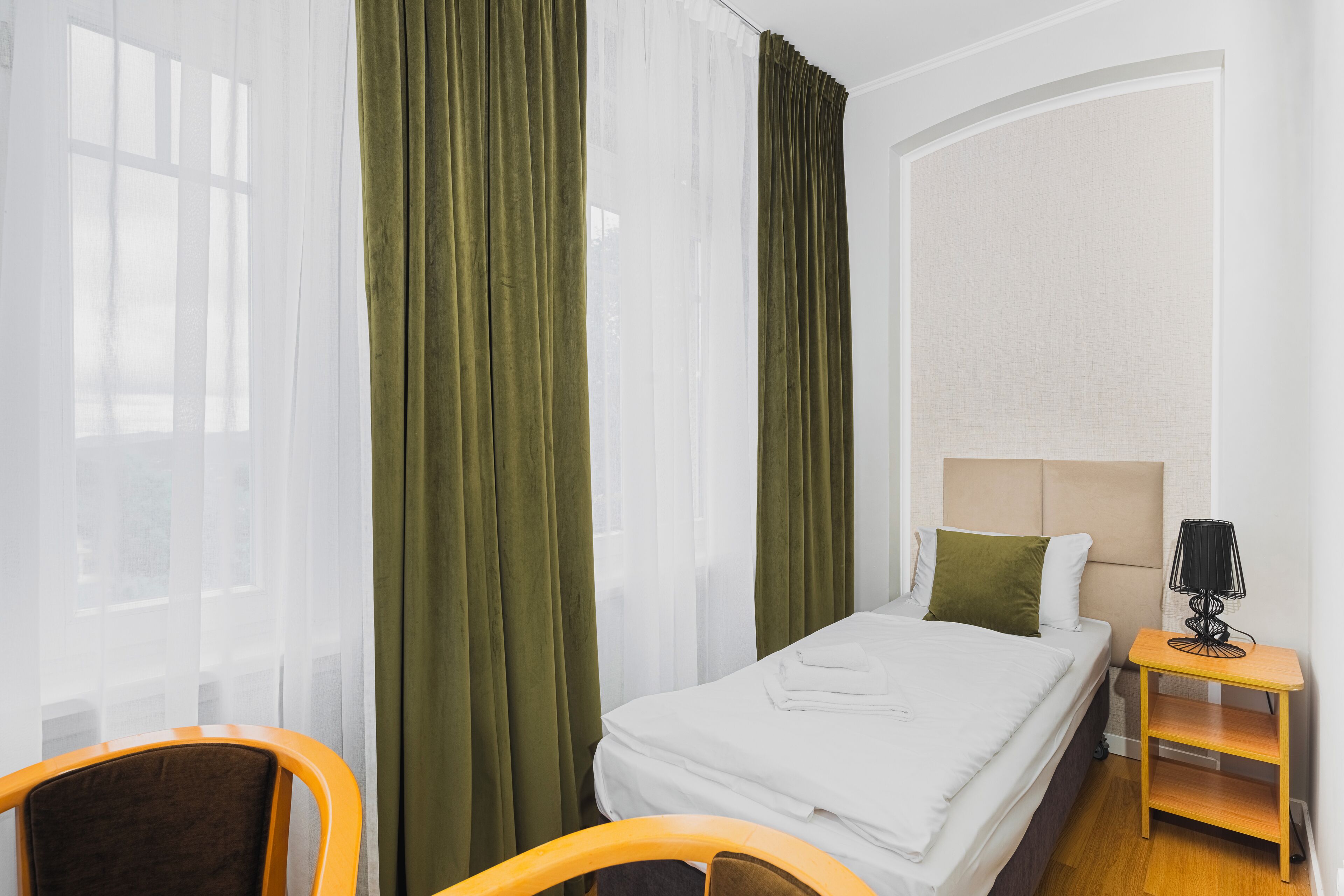 A hotel room with a bed, a chair, a nightstand, and sheer curtains.