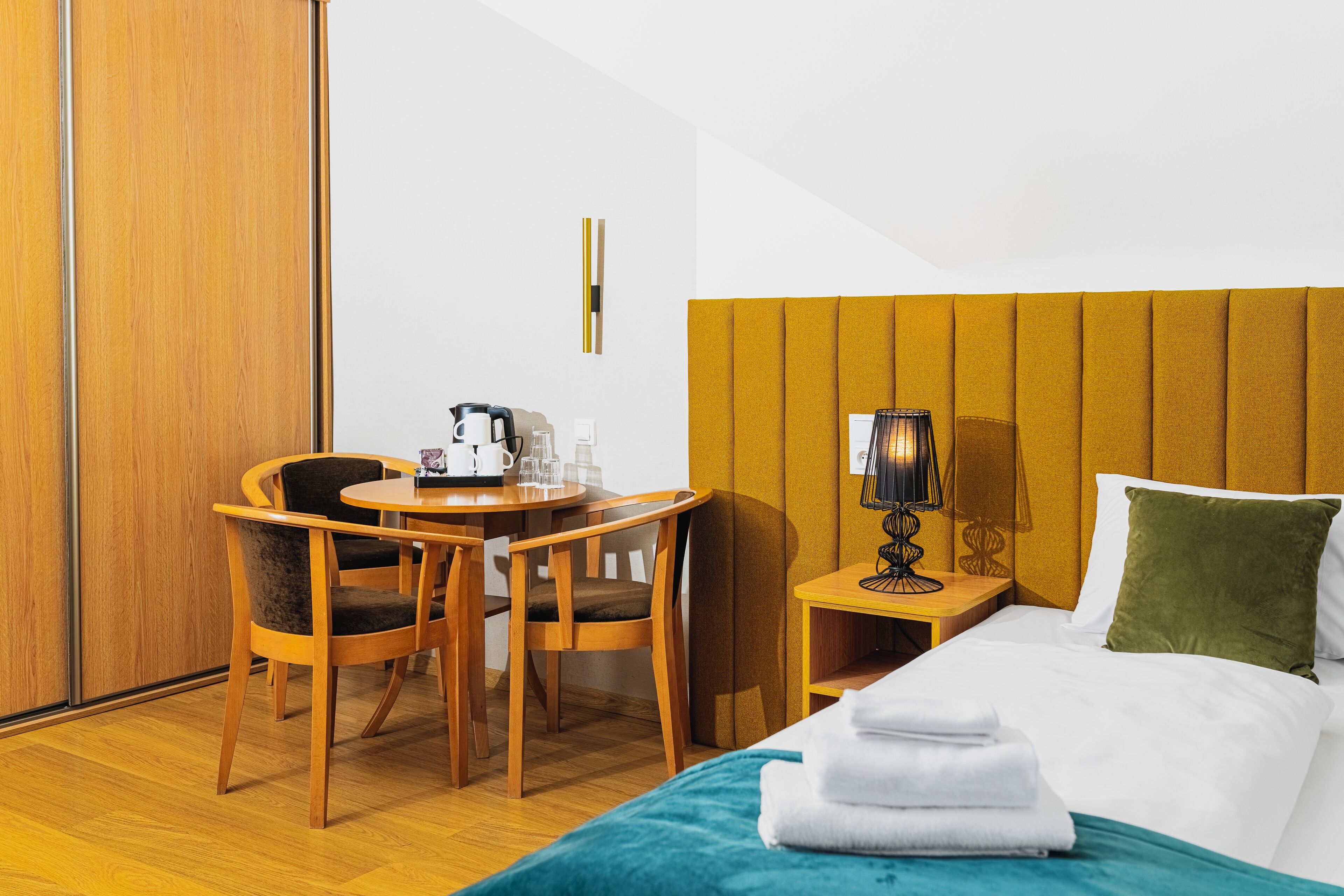 A hotel room with a bed, a desk with chairs, a coffee maker, and a lamp.