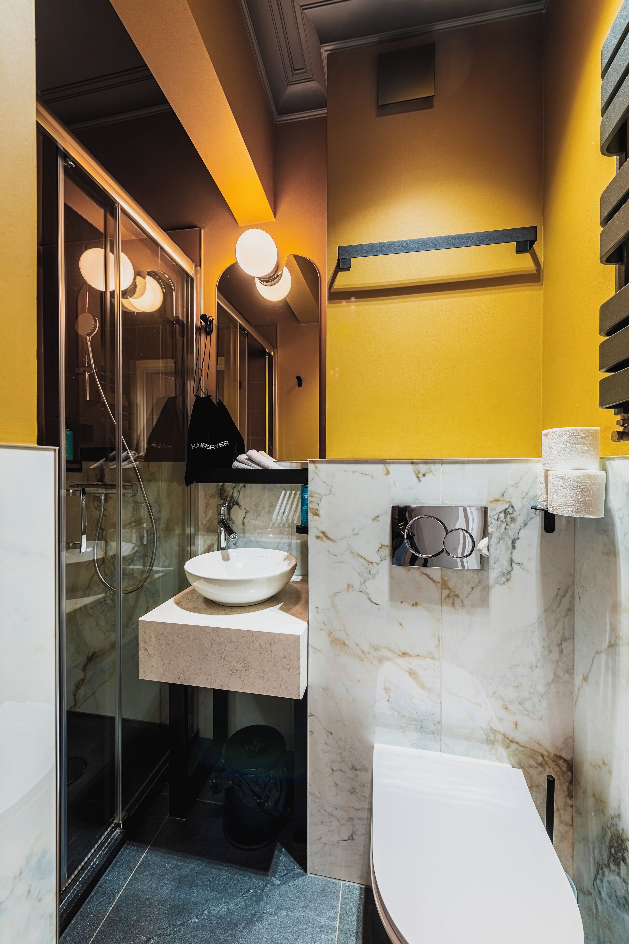 Un baño moderno con ducha envuelta en cristal, lavamanos de mármol y retrete.