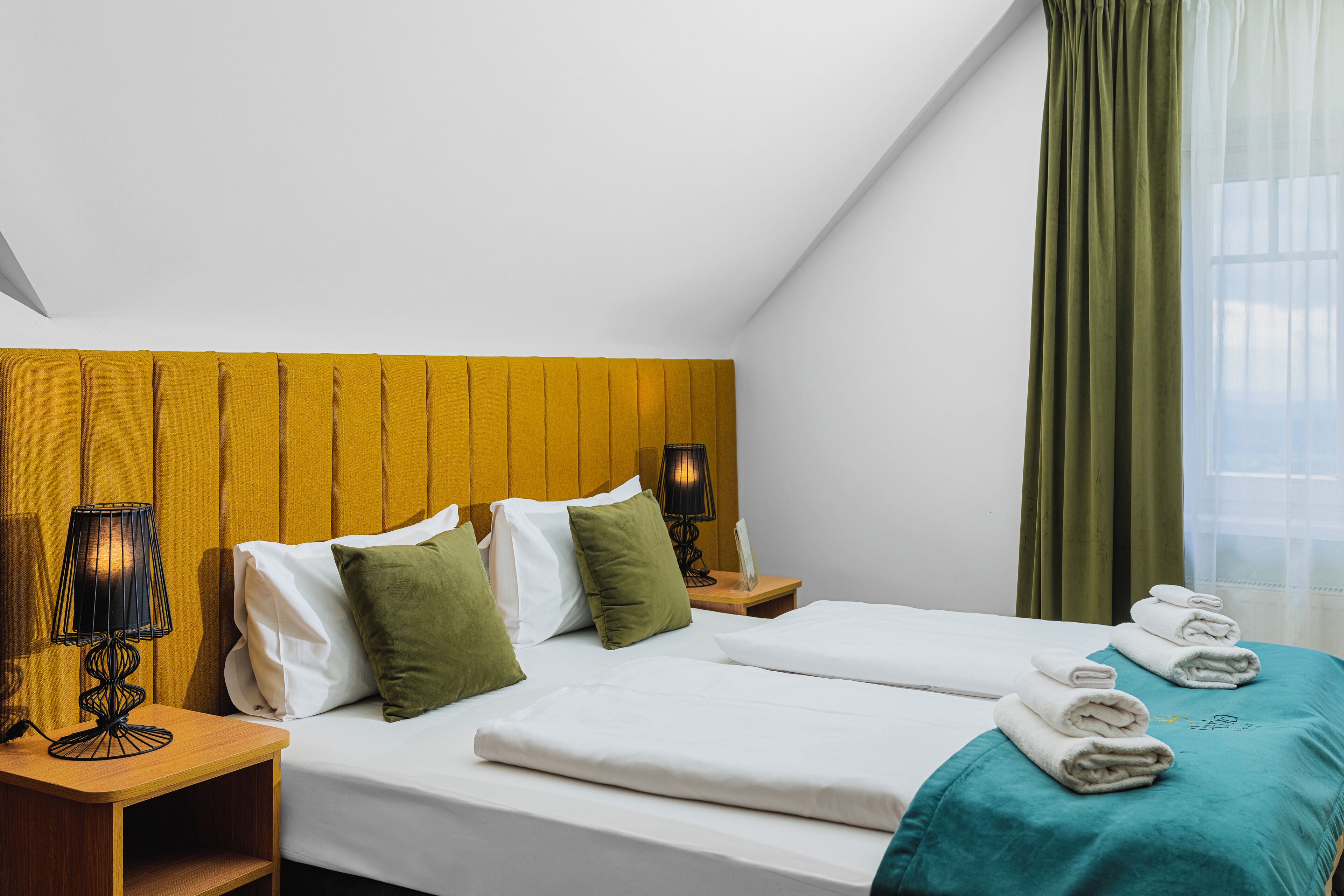 Une chambre d’hôtel avec deux lits, une tête de lit en bois, une table de chevet avec une lampe et une fenêtre avec des rideaux.