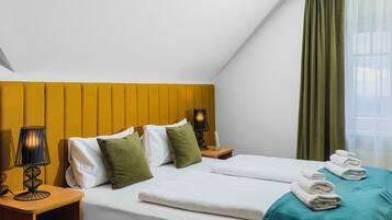 A hotel room with two beds, a wooden headboard, a nightstand with a lamp, and a window with curtains.