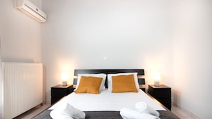 A hotel room with a bed, two nightstands with lamps, a radiator, and towels on the floor. - MTC-NS Apartments by the Airport (Markopoulo Mesogaias)