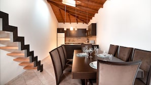A dining area with a wooden staircase, a kitchen in the background, and a table set for four. - MTC-NS Apartments by the Airport (Markopoulo Mesogaias)