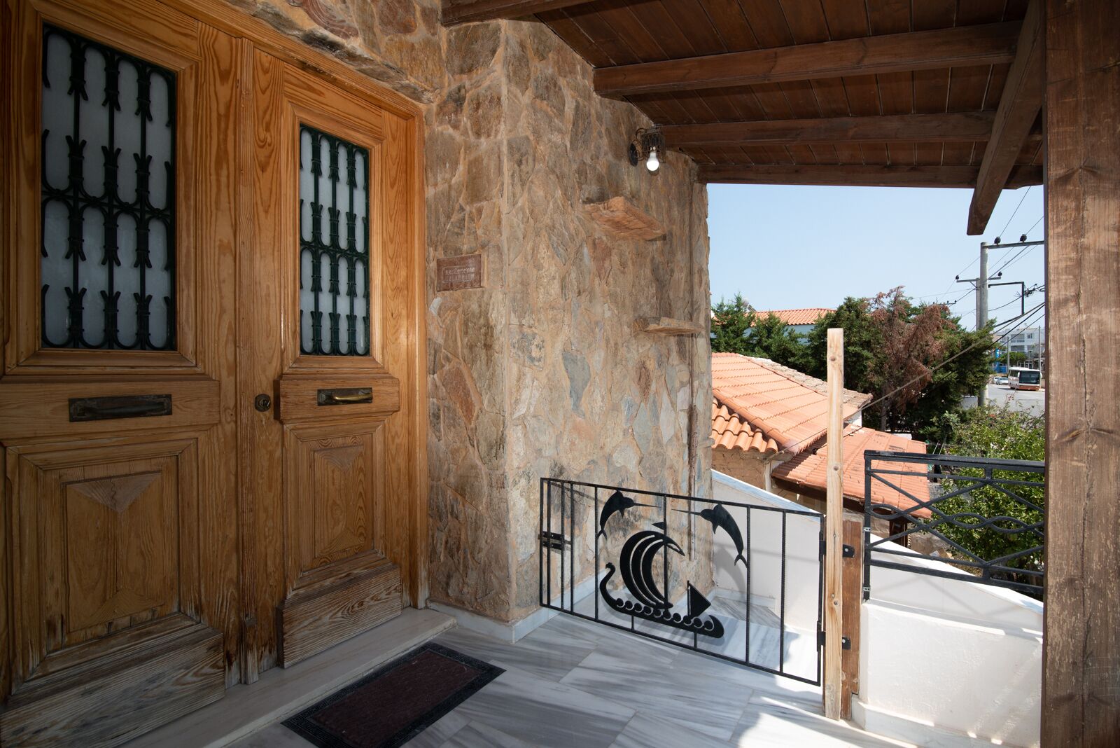 Una puerta de madera con paneles de vidrio, una pared de piedra y una barandilla de metal con diseño decorativo.