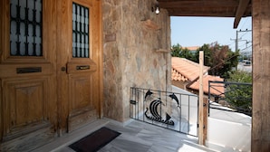 A wooden door with glass panels, a stone wall, and a metal railing with a decorative design. - MTC-NS Apartments by the Airport (Markopoulo Mesogaias)