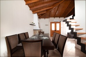 Un comedor con una mesa y sillas de madera, una cocina con estufa y un equipo de aire acondicionado, y una escalera de diseño moderno.