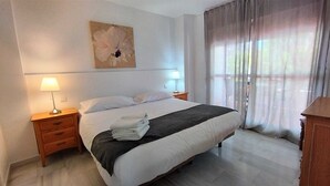 Habitación de hotel con cama, dos lámparas de noche, mesita de noche, toalla doblada y un cuadro en la pared.