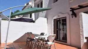 Un patio con una mesa y sillas, una sombrilla verde y un edificio blanco con techo de tejas.
