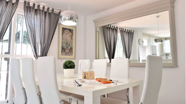 Un comedor con una mesa blanca, cortinas grises y una lámpara colgante.
