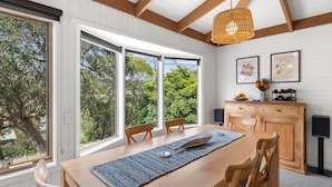 A dining area with a wooden table, chairs, and a large window offering a view of greenery. - Soulhaven (Anglesea)