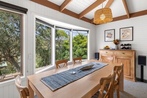 Espaço de refeições com mesa de madeira, cadeiras e uma janela grande com vista para o verde.