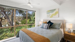 A bedroom with a large window, a bed with a headboard, bedside lamps, and a ceiling fan.