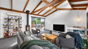 A modern living room with a high ceiling, built-in bookshelves, a fireplace, a television, and a cozy seating area. - Soulhaven (Anglesea)