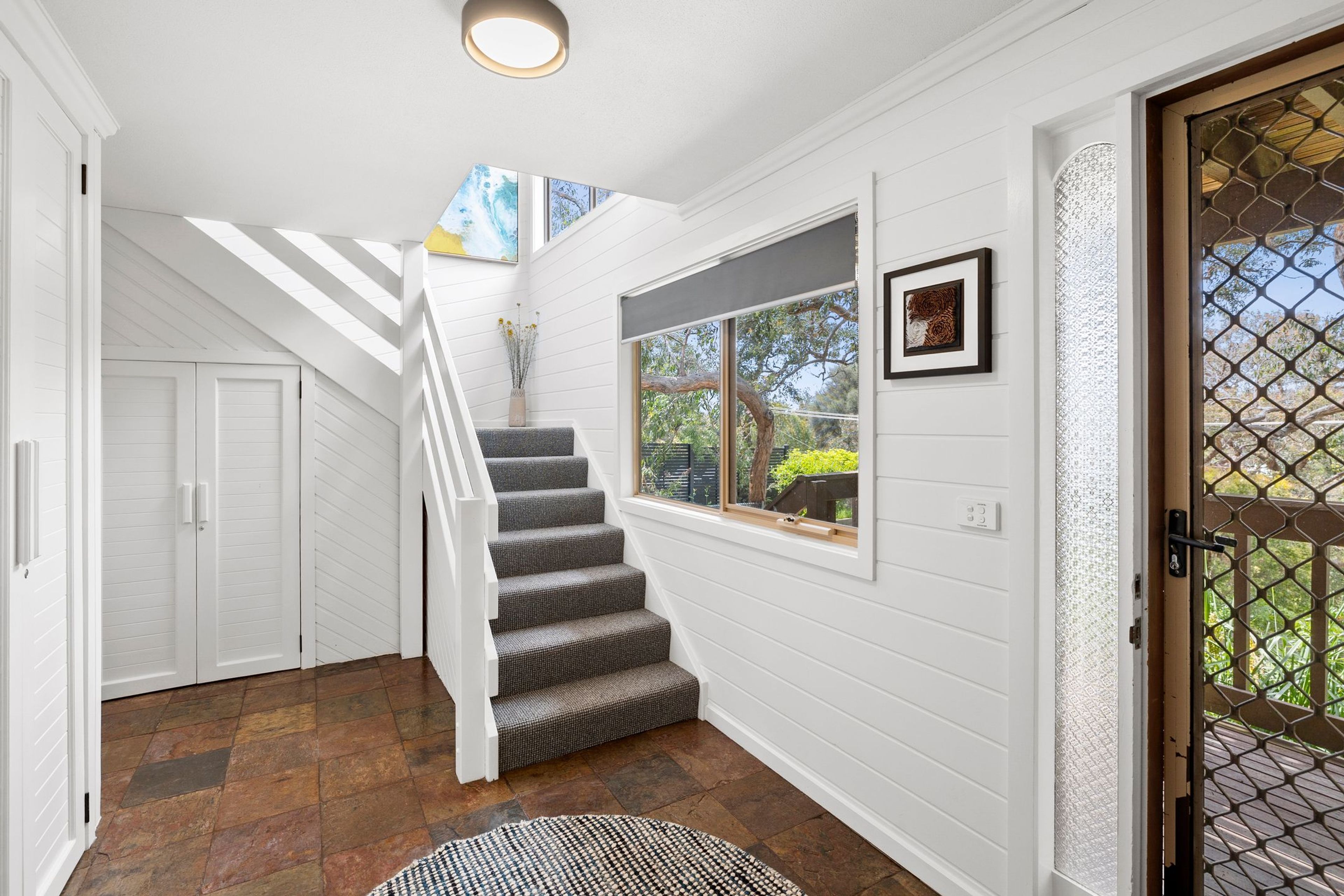 A staircase leading to a second floor with a view of the outdoors, a door with a glass panel, and a rug on the floor.