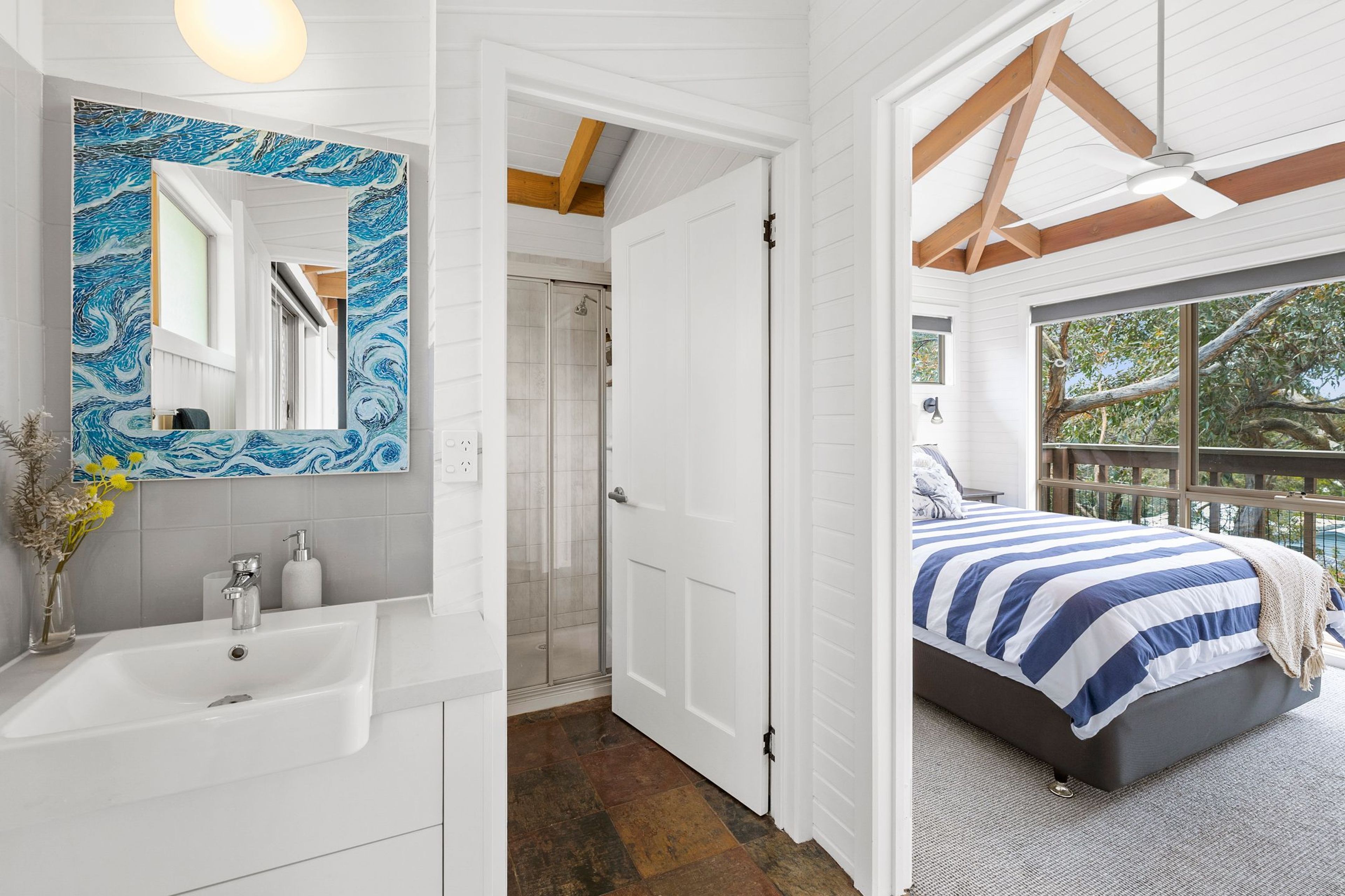 Een slaapkamer met een bed, een badkamer met een wastafel en een douche.