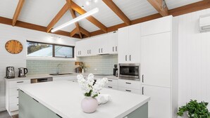 A modern kitchen with white cabinetry, a central island, and a large window above the sink. - Soulhaven (Anglesea)