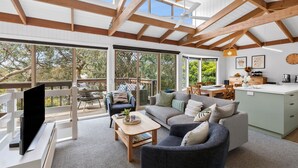 A spacious living area with a large sofa, a coffee table, and a television. There is a balcony with outdoor seating and a view of trees. - Soulhaven (Anglesea)