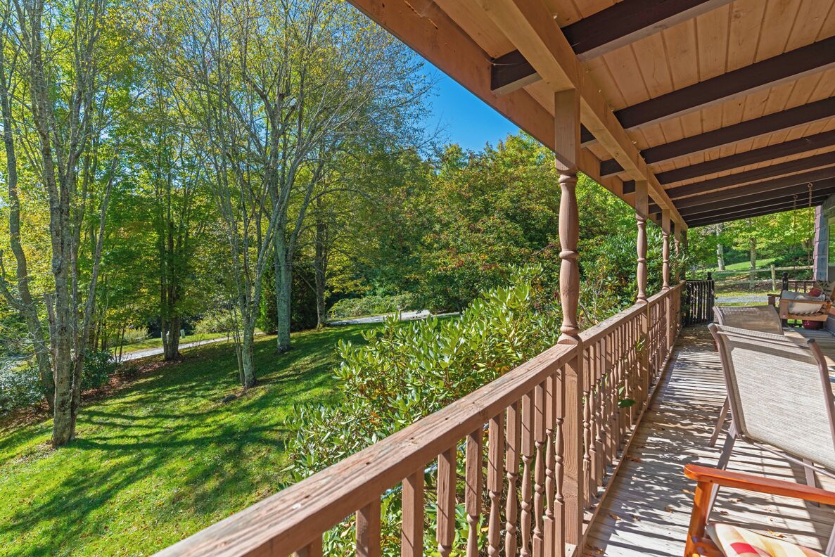 Une terrasse en bois dotée d’une rambarde, qui offre une vue sur un jardin bien entretenu et des arbres.