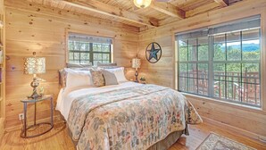 Ein Schlafzimmer einer Holzhütte mit Bett, zwei Fenstern, einem Deckenventilator und einer Sternen-Dekoration an der Wand.