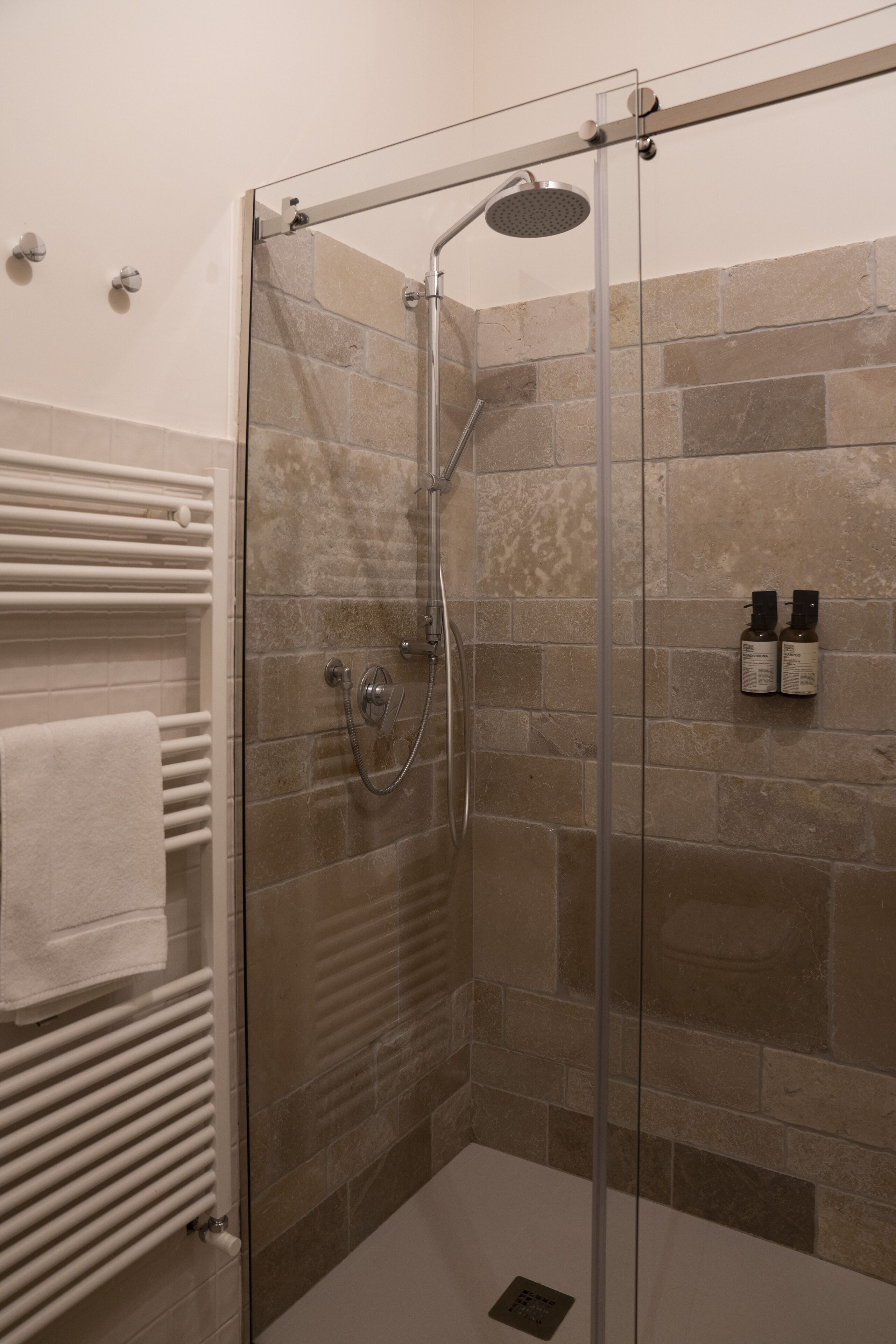 A glass-enclosed shower with a handheld showerhead and a wall-mounted faucet.