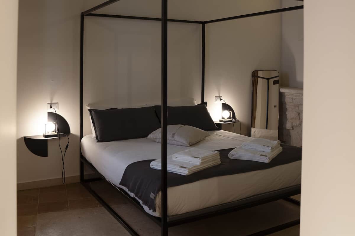 A four-poster bed with a canopy, bedside lamps, a mirror, and a small table.