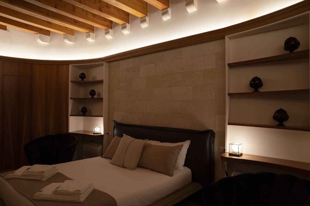 A hotel room with a bed, a chair, and shelves with decorative items.