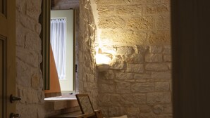 A narrow stone-walled room with a table and chairs, a window with curtains, and a wall-mounted TV. - Palazzo Vittoria (Bisceglie)