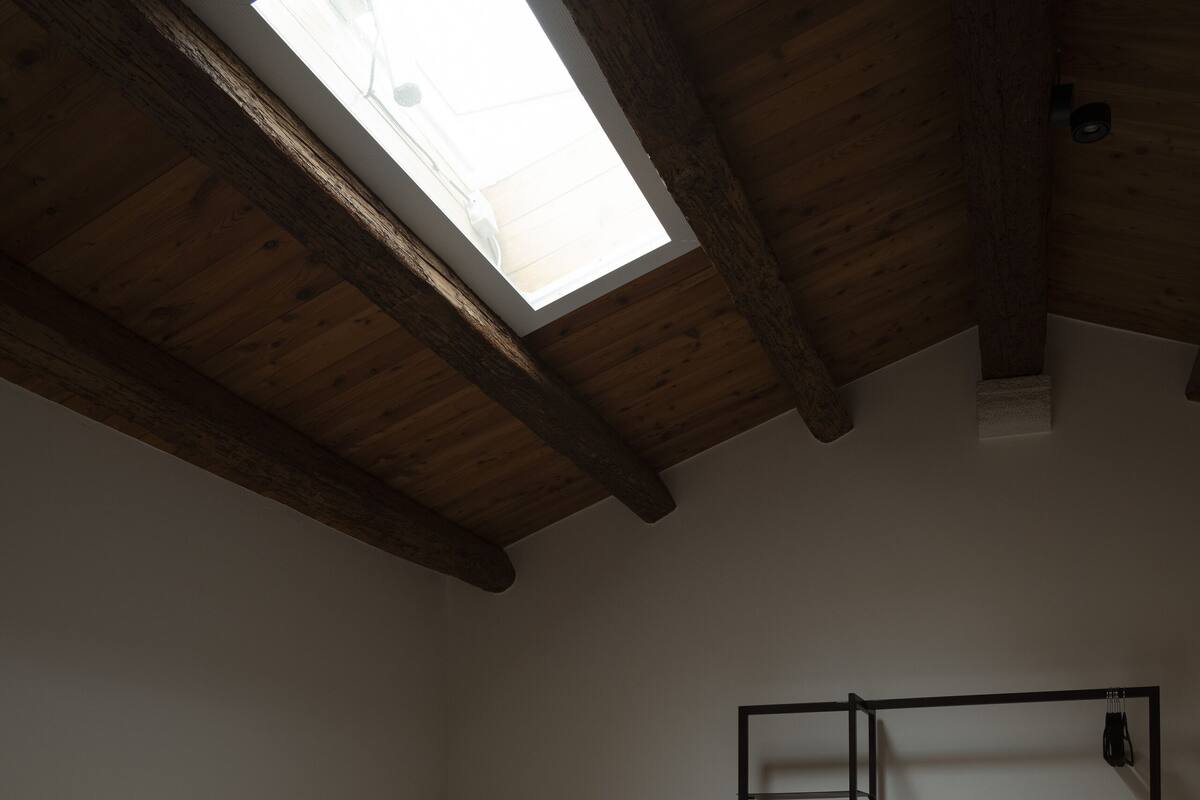 A bedroom with a skylight, a bed with white linens, a wooden headboard, a wardrobe, and a mirror.