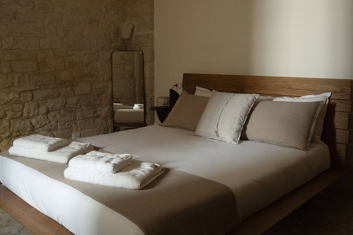 A bedroom with a stone wall, a wooden headboard, a bed with white linens, and a mirror on the wall.