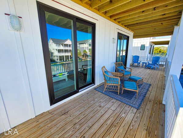 A wooden deck with wicker chairs and a blue rug. - Gone Coastal: A Paws-itively Perfect Beach Escape! (Surf City)
