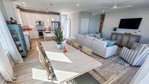A modern kitchen with white cabinets, stainless steel appliances, and a dining area with a wooden table and chairs. - Gone Coastal: A Paws-itively Perfect Beach Escape! (Surf City)