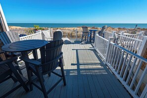 A wooden deck with outdoor seating, including tables and chairs, overlooking a beach. - Comfy, spacious 3 bedroom oceanfront townhouse with free WiFi and breathtaking ocean views located downtown just steps from the beach! (Ocean City)