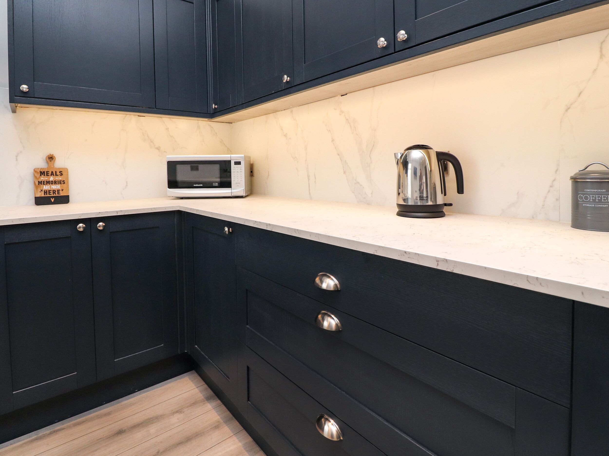 A kitchen with dark cabinets, a microwave, a kettle, and a coffee can.