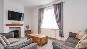 A living room with a fireplace, a television mounted on the wall, and a large window with curtains. - 37 Nutter Road (Thornton-Cleveleys)