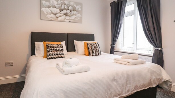 A neatly made bed with white linens, two pillows with geometric patterns, and a folded towel on the bed. - 37 Nutter Road (Thornton-Cleveleys)
