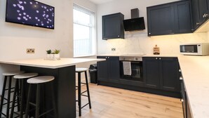 A modern kitchen with black cabinets, a large island with stools, a microwave, and a TV displaying heart patterns. - 37 Nutter Road (Thornton-Cleveleys)