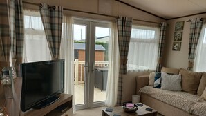 Ett vardagsrum med en platt-TV på ett träställ, en beige soffa med mönstrade kuddar och ett soffbord i glas.