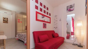 A room with a red sofa, a bed with a floral bedspread, a mirror, and a wall with framed pictures.