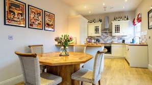 A dining area with a wooden table and wicker chairs, a kitchen with white cabinets, and a backsplash of white tiles. - Apartment 4 - The Kings -  a family break that sleeps 4 guests  in 2 bedrooms (York)