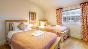 A hotel room with two beds, each with patterned bedding and pillows, a bedside table with a lamp, and a window with curtains. - Apartment 4 - The Kings -  a family break that sleeps 4 guests  in 2 bedrooms (York)