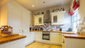 A kitchen with white cabinets, a wooden countertop, a built-in oven, and a window with curtains. - Apartment 4 - The Kings -  a family break that sleeps 4 guests  in 2 bedrooms (York)