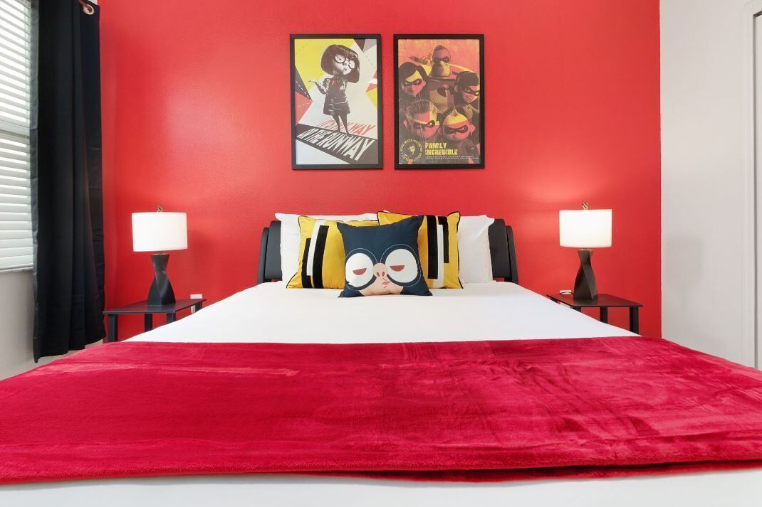 A bedroom with a red wall, white bedspread, two lamps, and two framed posters.