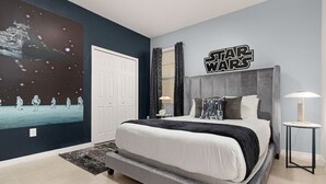 Un dormitorio con una pared temática de Star Wars, una cama grande y una mesita de noche con lámpara.