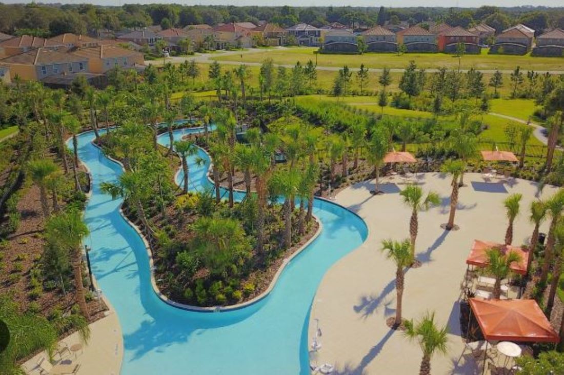 Um resort com piscina sinuosa, palmeiras e guarda-sóis de praia.