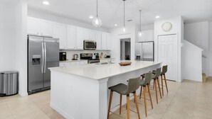 Una cocina moderna con armarios blancos, electrodomésticos de acero inoxidable y una isla central con taburetes de bar.