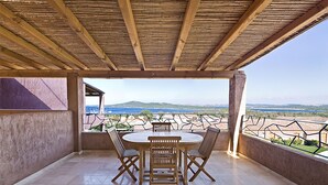 A covered patio with a round table and four chairs, overlooking a scenic view of hills and a body of water. - Apartment with beautiful sea view (Santa Teresa Gallura)