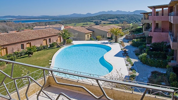 A pool surrounded by buildings with a view of mountains and a body of water. - Apartment with beautiful sea view (Santa Teresa Gallura)